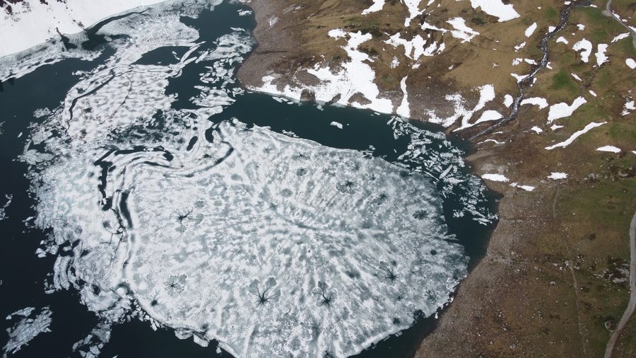 Partially icy Formarin Lake surrounded by Alpine mountains